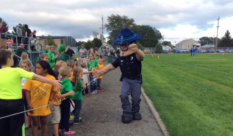 An Officer Mascot gives high fives to children in crowd