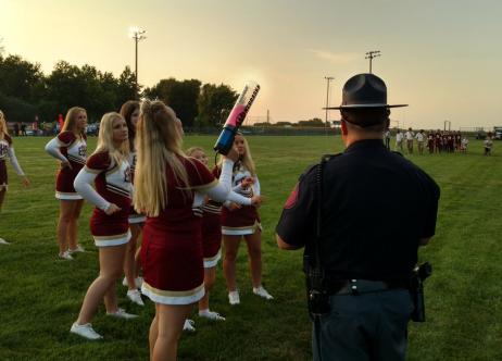 high school cheerleaders on football field with patrol officer standing nearby